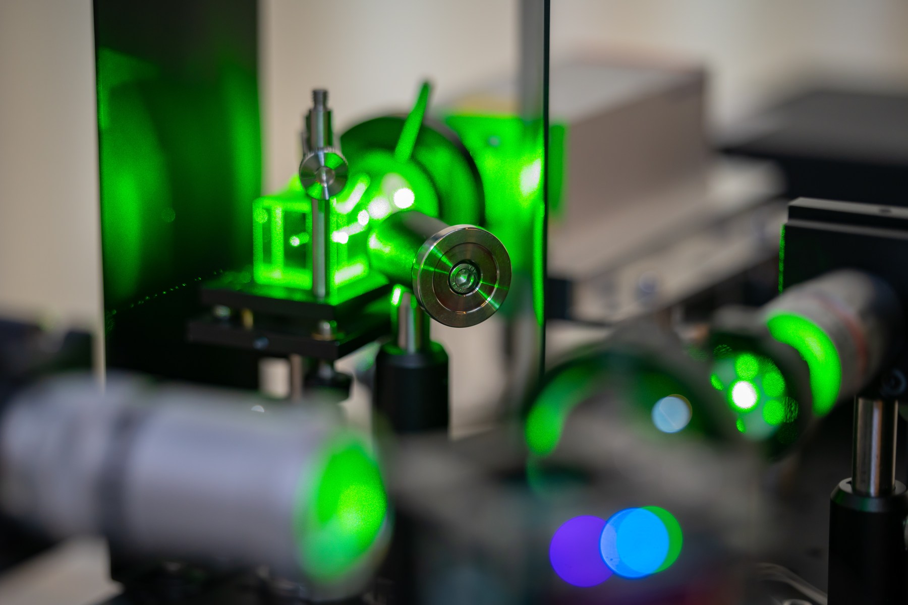 Green light interacting with optical components in a PhotonicsAI experimental setup.